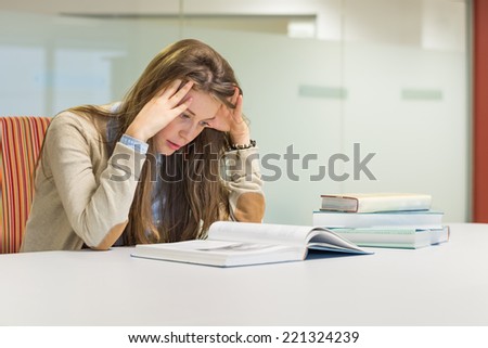 Stressed female student in the university library reading books. Young attractive woman studying for exam. Education concept