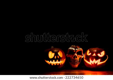 Scary Halloween pumpkins and skull isolated on a black background with room for text. Scary glowing faces trick or treat