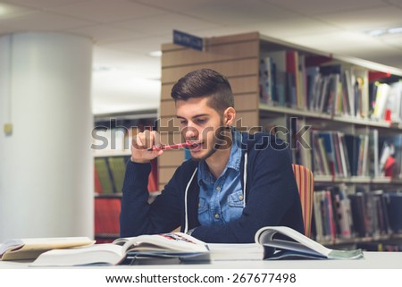 Portrait of good looking male student reading and doing research in the library. Lifestyle image of university student studying for exam with a vintage, blue filter applied. Knowledge is power concept