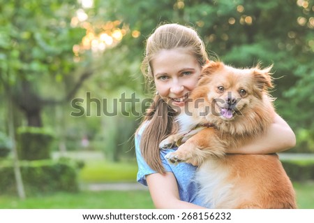 Lifestyle image of cute young woman holding dog and smiling. Loving dog in his owner\'s arms in the park. Concept of caring for a pet and animal adoption. Image with copy space for adding text or quote