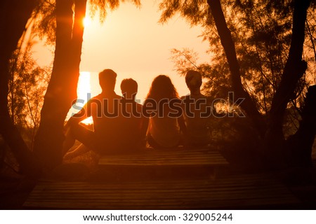 Silhouette of a family sitting down and watching the sun setting over the sea. People relaxing at the seaside during holiday and enjoying a beautiful sunset together.
