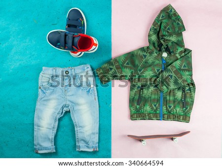 Stylish outfit for little skater boys with denim jeans, green jacket and blue sneakers. Kids fashion clothes on a blue and pink background with a toy skateboard. Tiny clothes for boys