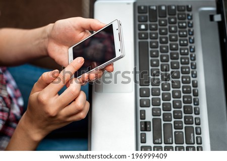 Hands with cell phone in front of laptop