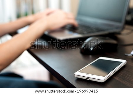 Cell phone on the table near woman working on the laptop