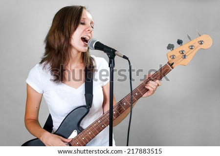 Girl singing with microphone and bass guitar isolated on gray background