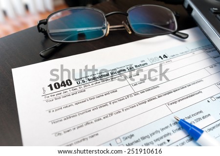 Filling Individual tax return form 1040 on a table with glasses, pen and laptop