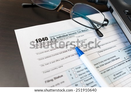 Individual tax return form 1040 on a table next to glasses, pen and laptop