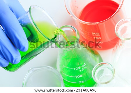 Researcher pouring the green solution from the beaker into the flask.
