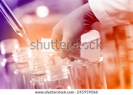 Gloved hand pour the solution from flask to test tube in laboratory.