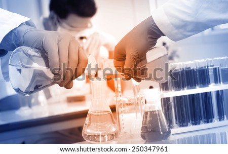 Gloved hand pour the solution from flask to another flask  in laboratory.