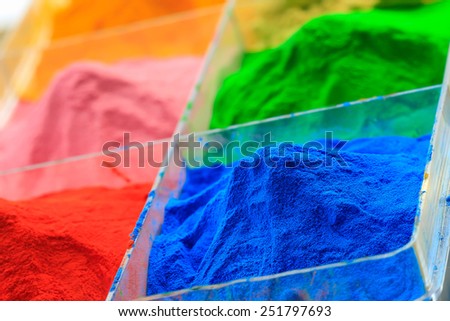 The pile of powder coating in plastic box, on wooden background.