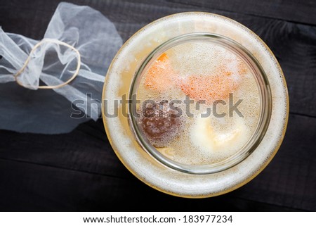 Fermented water kefir with grains on the bottom of jar and a floating piece of dry fruits