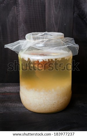 Fermented water kefir with grains on the bottom of jar and a floating piece of dry fruits