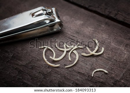Nail clipper and some nail clippings over a dark wooden surface
