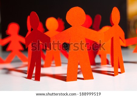 Group of paper doll holding hands. Teamwork concept paper craft. Orange dolls on black wooden background