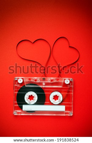 Vintage audio cassette with loose tape shaping two hearts on red background