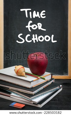 Apple on books and time for school handwritten on the chalkboard in the background