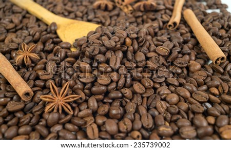 Lots of coffee beans. Two anise stars, three sticks of cinnamon. Wooden spoon. Shallow depth of field.