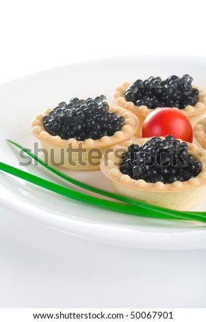 Tartlet with black caviar on a white platter, decorated with cherry tomatoes and green onions