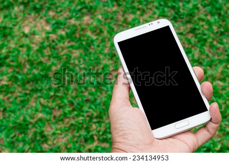 blank screen mobile phone in hand on green grass background