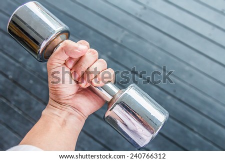 Hand holding steel dumbbell on black wood background