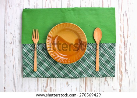 Wooden cutlery and blank disk on tablecloth over wooden table
