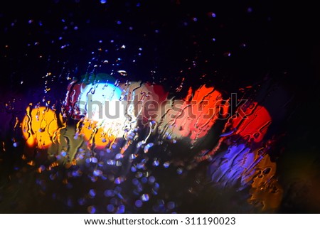 blurred rain drops on car glas with bokeh of light traffic