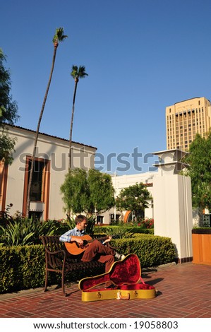 Young man playing guitar for money in a train station courtyard.