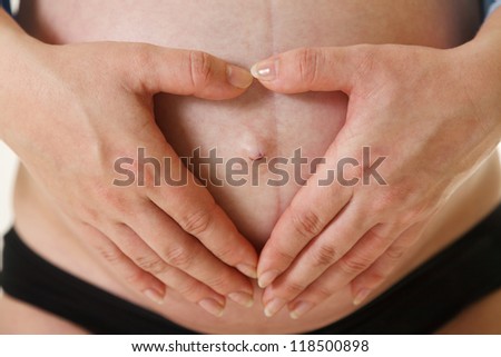 Heart shape made from hands on pregnant woman stomach.