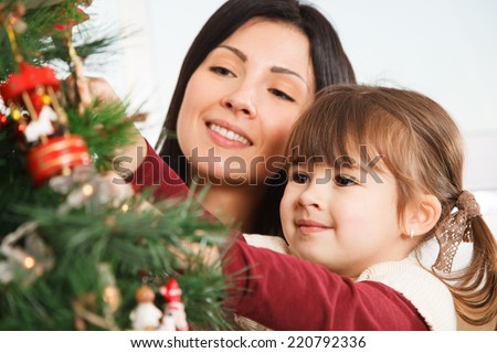A young girl helps her mother to decorate the family Christmas tree