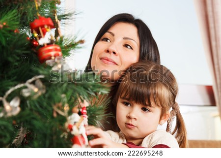 A young girl helps her mother to decorate the family Christmas tree.