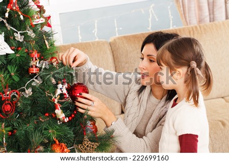 A young girl helps her mother to decorate the family Christmas tree.