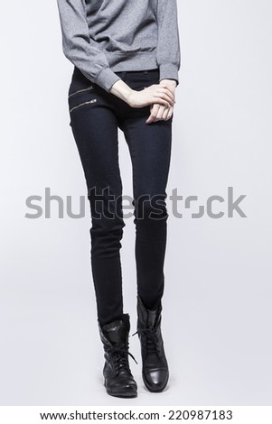 Front view of a standing woman(female) model wearing black denim(trousers) with boots and grey top isolated on a white background