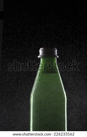 A green glass container with carbonated soft drink and water vapor on isolated black.