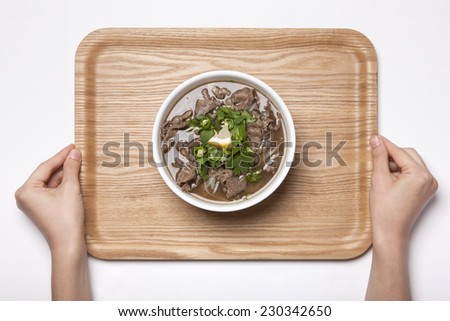 A female hands hold wood tray with a Vietnam rice noodles with beef isolated white, top view at the studio.