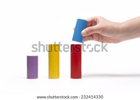 A female(woman) hand pick up(hold) a wood block among Color wood cylinder blocks(yellow, red, blue, purple) like bar graph symbolizing sales growth isolated white at the studio.