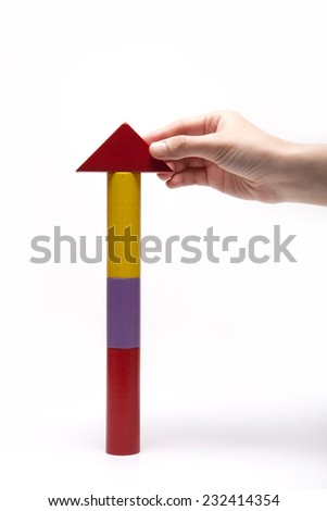 A female(woman) hand pick up(hold) a wood block among the tower(arrow, house) made with a color wood blocks symbolizing sales growth isolated white at the studio.