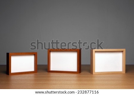 three empty(blank) wood photo frames(teak, cherry, oak) on the wood table(desk) at the studio.