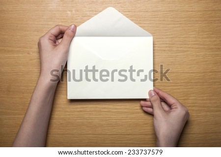 A female hands hold(grip) a white envelope on the wooden desk, top view at the studio.