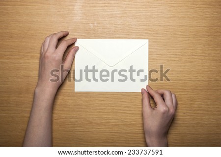 A female hands hold(grip) a white envelope on the wooden desk, top view at the studio.