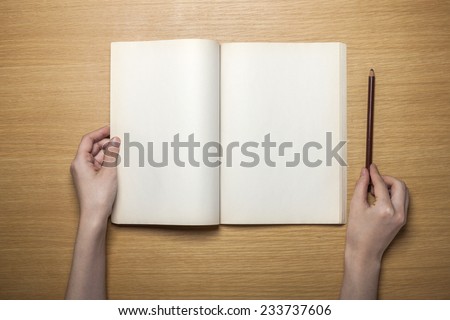 A female hands hold(grip) a vintage(old) book(note, diary) spread on the wooden desk with pencil, top view at the studio.