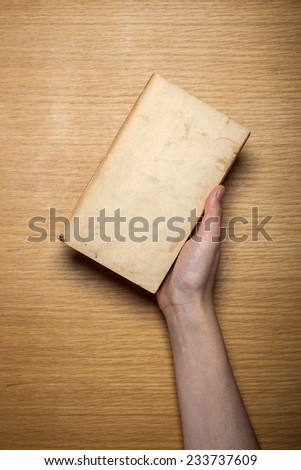 A female hand hold(grip) a vintage(old) book(note, diary) on the wooden desk, top view at the studio.