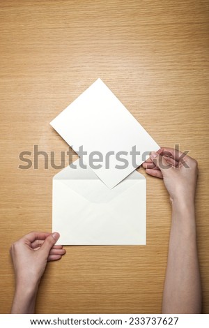 A female hands hold(grip) a white envelope and postcard on the wooden desk, top view at the studio.