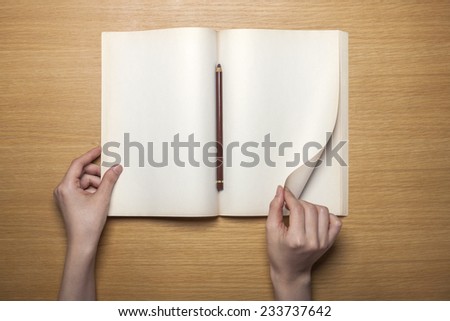 A female hands hold(grip) a vintage(old) book(note, diary) spread and through the pages of a book on the wooden desk with pencil, top view at the studio.