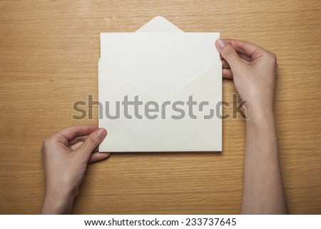 A female hands hold(grip) a white envelope and postcard on the wooden desk, top view at the studio.