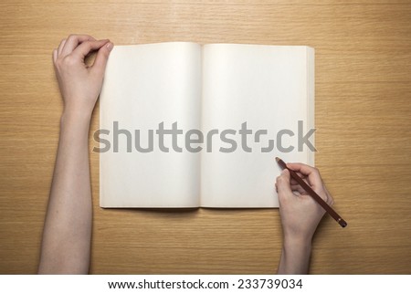 A female hands hold(grip) a vintage(old) book(note, diary) spread on the wooden desk with pencil, top view at the studio.