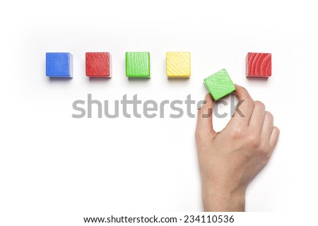 A female hand hold(pick up) green wood block among the color wood blocks isolated white, top view at the studio.