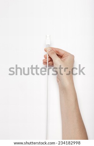 A female(woman) hand hold a white usb cable(jack, plug, socket) isolated white, top view at the studio.