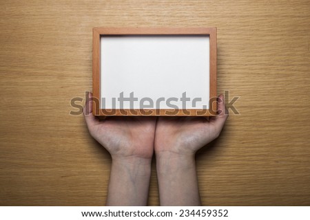 A female(woman) hands hold a wood photo(picture) empty(blank) frame on the desk at the studio.