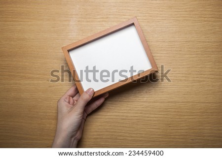A female(woman) hands hold a wood photo(picture) empty(blank) frame on the desk at the studio.